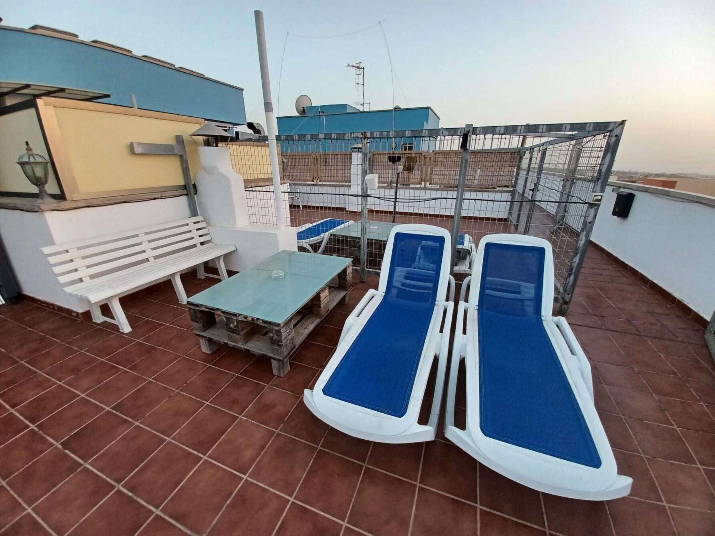 Una terrazza sul tetto con un tavolo, due poltrone, una panca e un recinto in metallo.