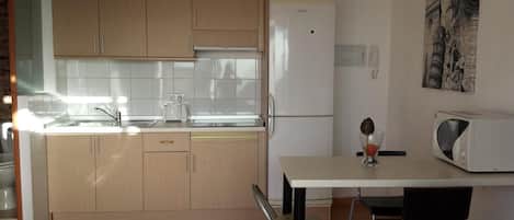 Une cuisine compacte avec des meubles en bois, un réfrigérateur blanc, un four à micro-ondes et une petite table à manger avec une chaise.