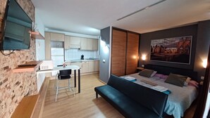 Quarto moderno com uma cama, escrivaninha e cozinha compacta.