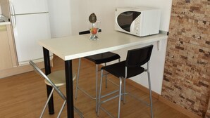 Uma kitchenette compacta com bancada branca, micro-ondas e uma pequena mesa com duas cadeiras.