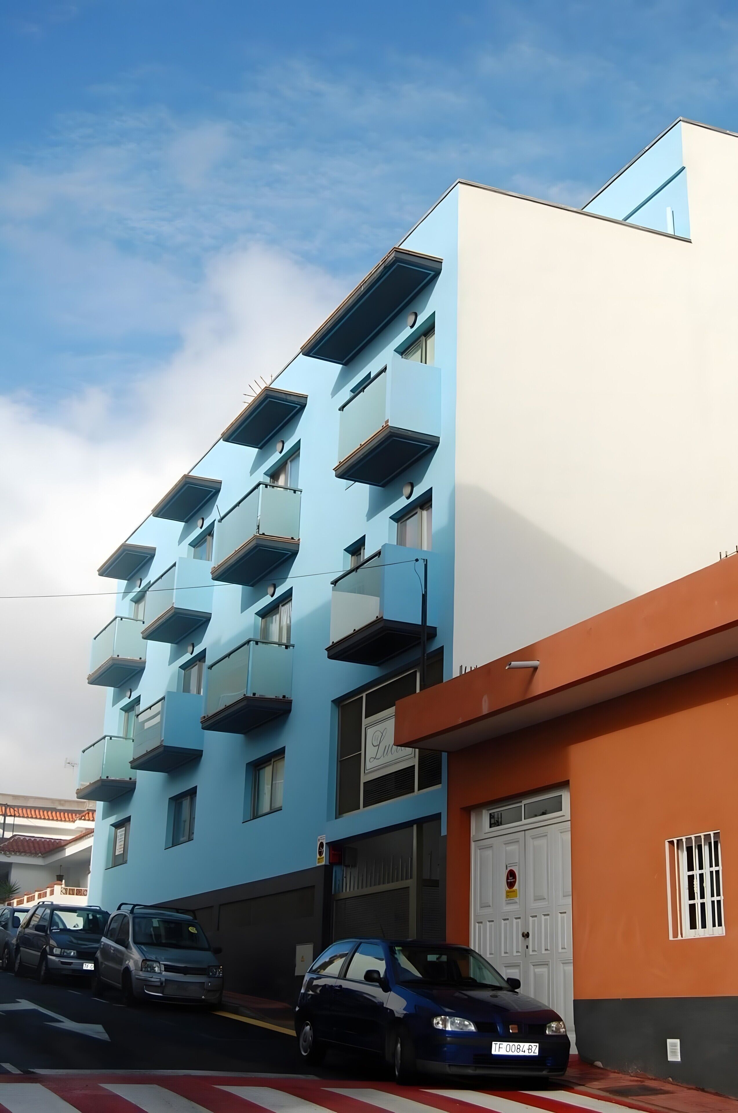 A multi-story building with balconies, a garage door, and parked cars.