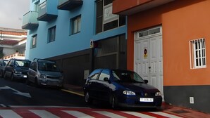 Um edifício com várias andares, varandas, uma porta de garagem e carros estacionados.