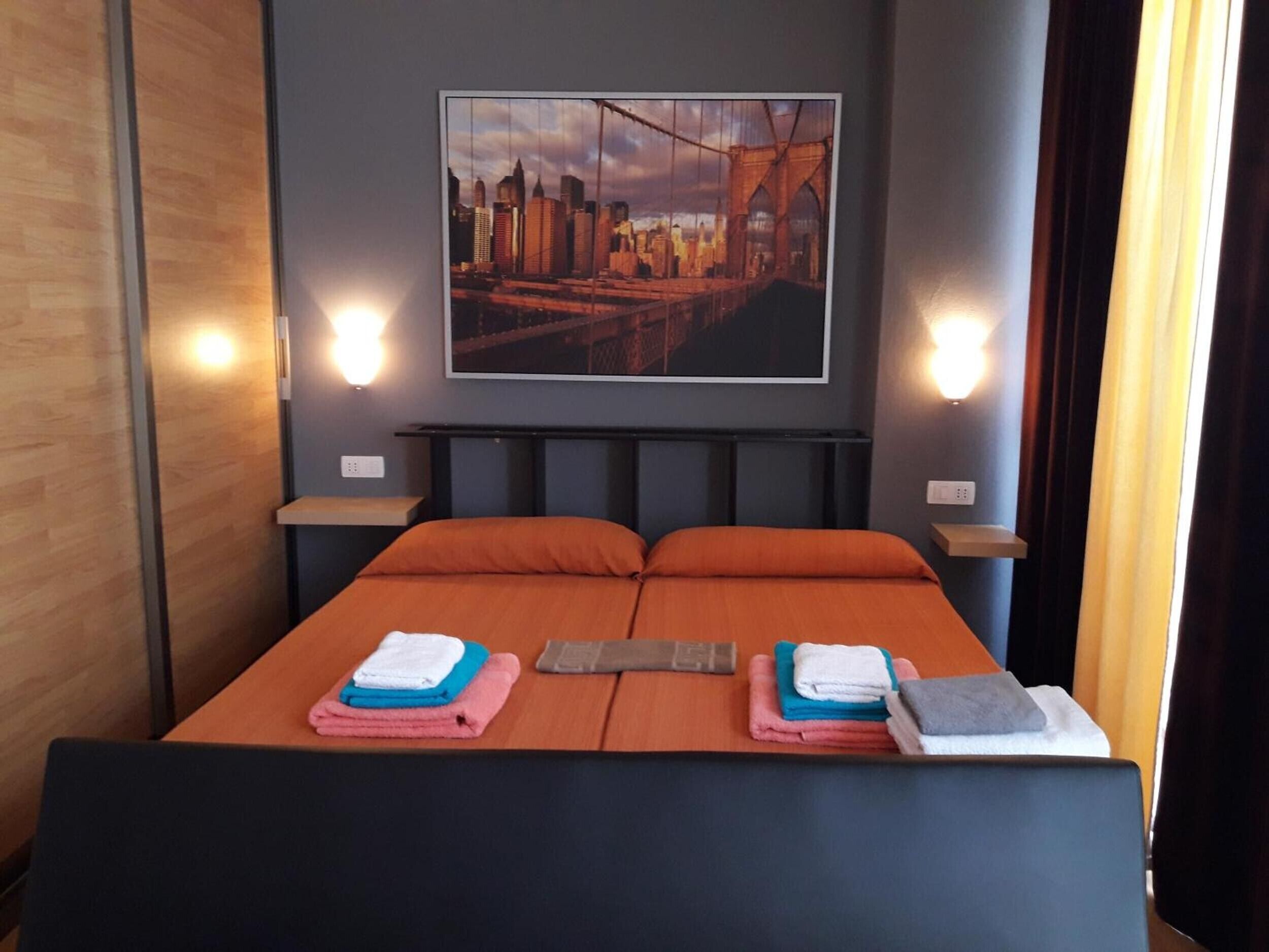 Hotelkamer met een bed, twee nachtkastjes, een stadsgezicht schilderij en wandlampen.