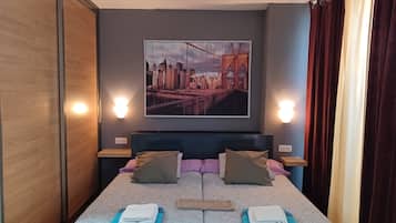 Une chambre d’hôtel avec un lit, des oreillers, un tableau représentant un paysage urbain, des lampes de chevet et des rideaux.