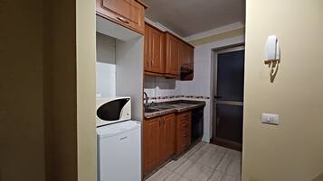 A compact kitchen with wooden cabinets, a microwave, and a built-in oven.