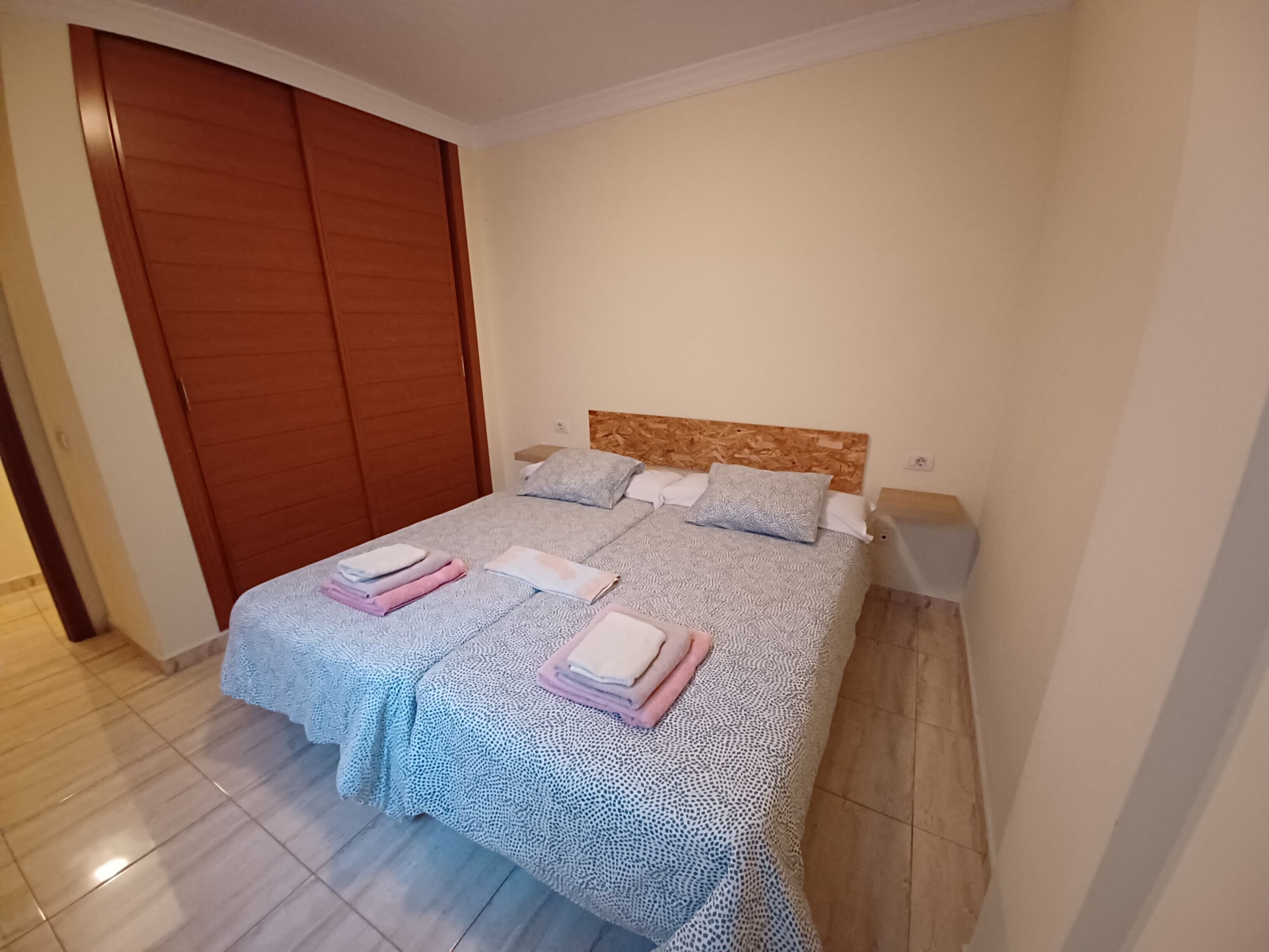 A neatly made bed with a patterned bedspread and pillows, a wooden headboard, and a wooden wardrobe.