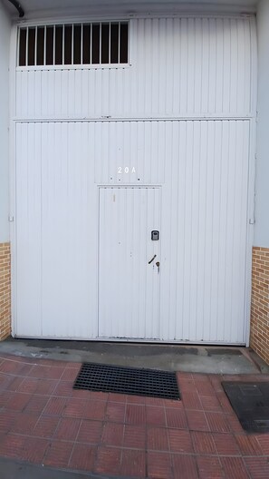 Een witte garage deur, gesloten, met een keypad slot, een klein raam en het nummer '20A' op de deur.