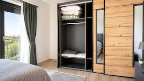 Ein Schlafzimmer mit einem Bett, einem Kleiderschrank, einem Spiegel und Blick ins Freie.