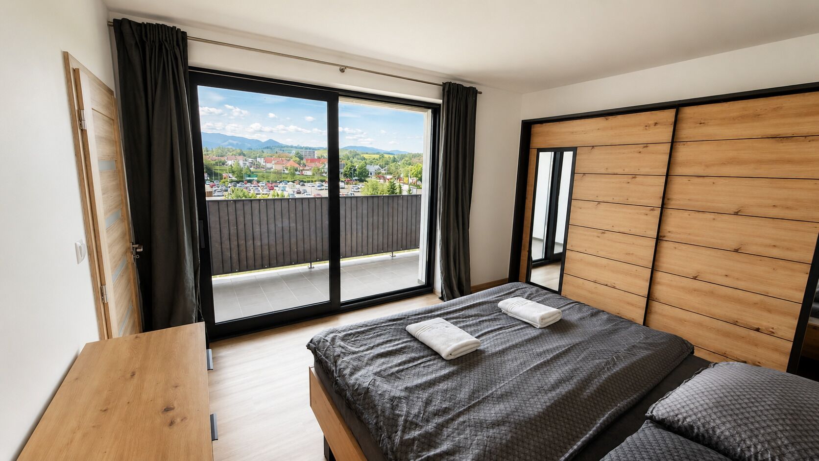 Un dormitorio con cama, cabecera de madera, vista a través de un ventanal y puerta corrediza que da a un balcón exterior.