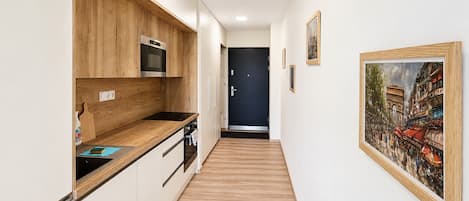 A narrow hallway with a kitchen on one side, featuring wooden cabinets and a microwave.