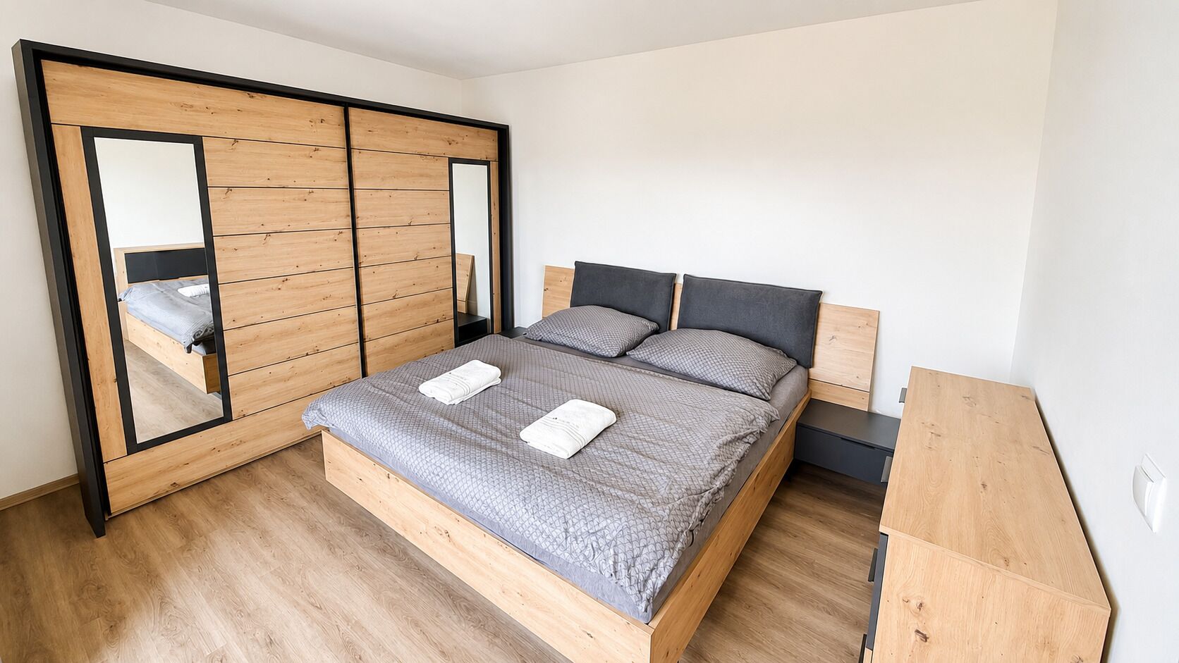 Een slaapkamer met een bed, een garderobe met spiegel en een nachtkastje.