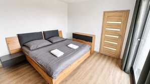 A modern bedroom with a wooden bed, grey bedding, a nightstand, and a wooden wardrobe. - Modern 2 room apartment with terrace, Chrenoviská (Liptovský Mikuláš)
