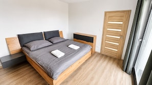 Ein modernes Schlafzimmer mit einem hölzernen Bett, grauer Bettwäsche, einem Nachttisch und einem Holzschrank.