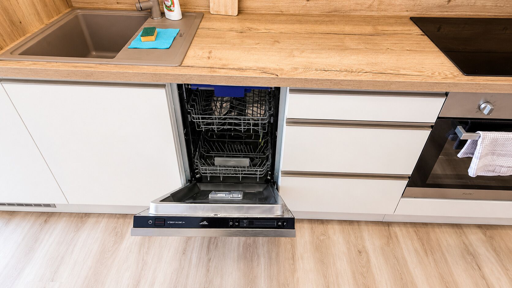Une cuisine moderne dotée d’un lave-vaisselle intégré, d’un plan de travail en bois et de meubles de rangement blancs.