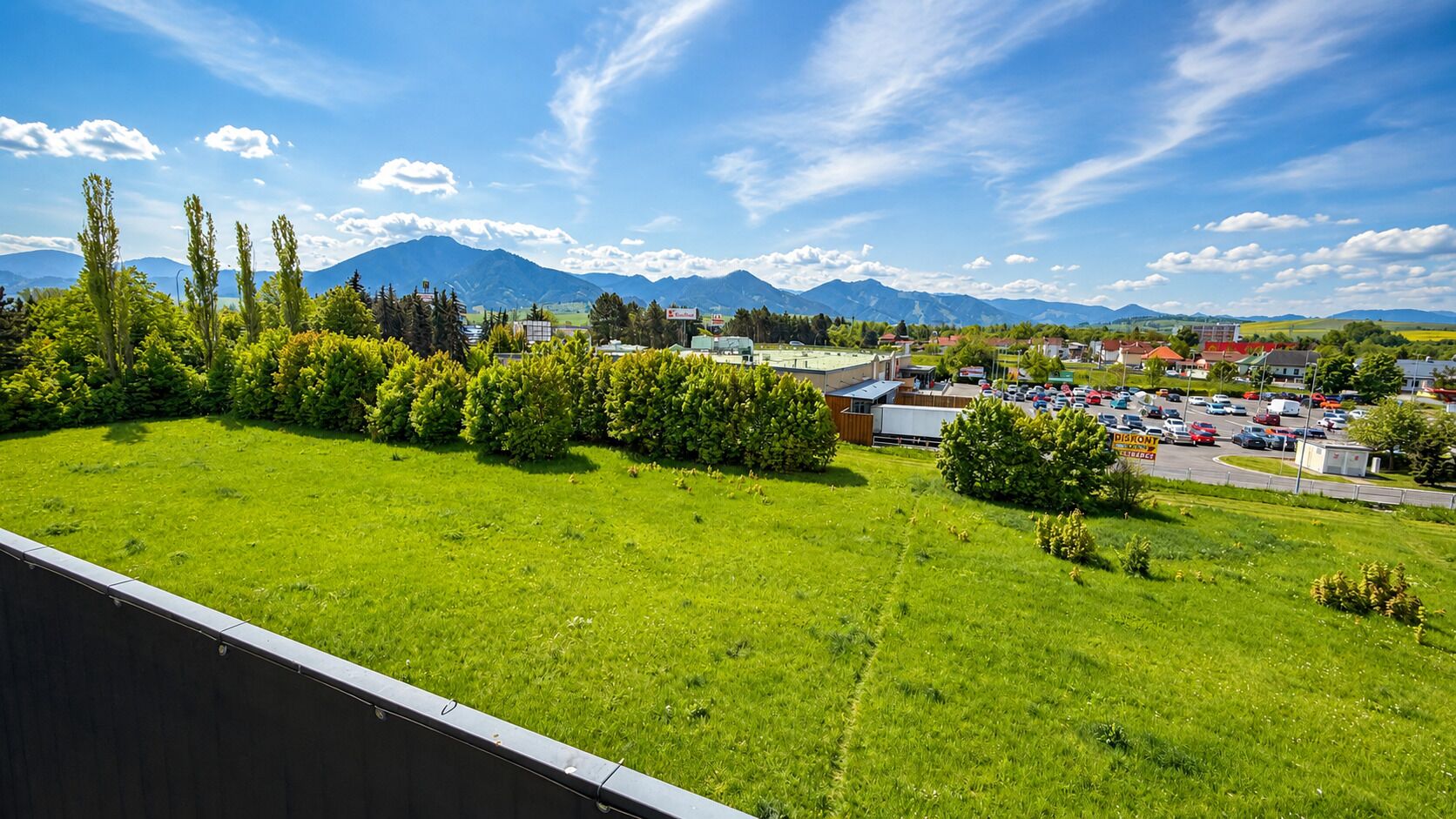 A green field with a parking lot and buildings in the background.