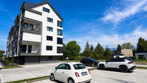 A modern multi-story building with balconies, a parking lot with cars, and trees in the background. - Modern 2 room apartment with terrace, Chrenoviská (Liptovský Mikuláš)