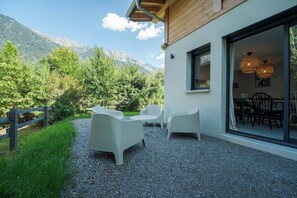 A modern outdoor seating area with white chairs and a table, a wooden deck, and a mountain backdrop. - Cimes - Modern, Sleeps 8 | New | Family-Friendly | Quiet Location (Chamonix)