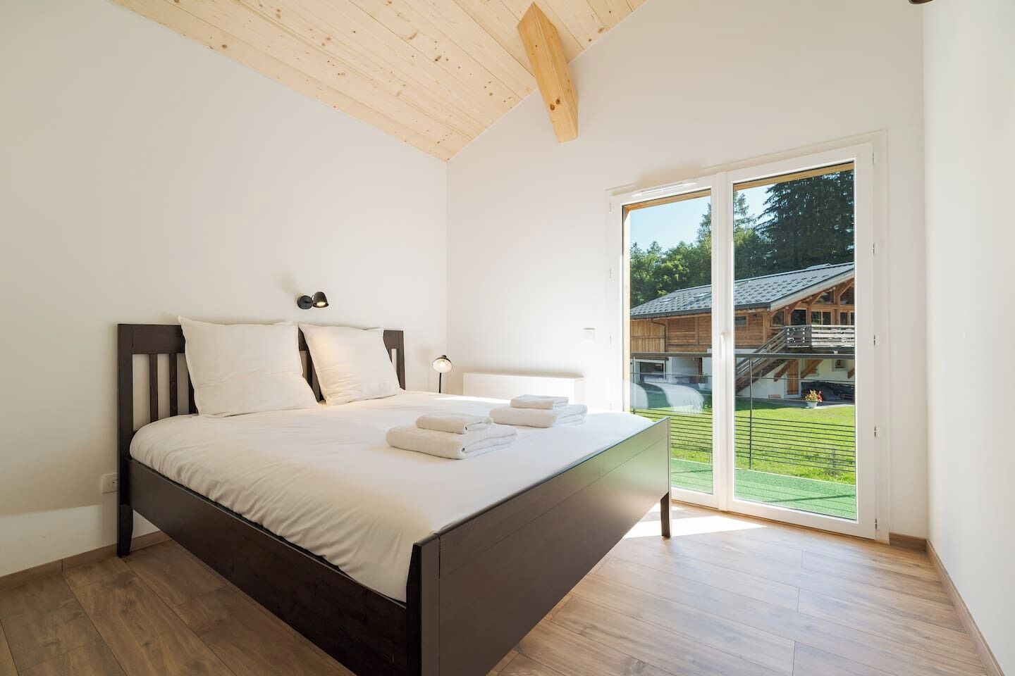 A bedroom with a bed, a nightstand, a wall-mounted lamp, and a sliding glass door leading to an outdoor area.