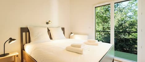 A bedroom with a large bed, bedside lamps, and a view of greenery through a sliding glass door.