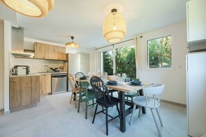 A modern kitchen with wooden cabinets, a dining table set for four, and large windows offering a view of greenery. - Cimes - Modern, Sleeps 8 | New | Family-Friendly | Quiet Location (Chamonix)