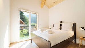 Une chambre à coucher avec un lit, des tables de chevet et une vue sur un jardin, accessible par une porte coulissante.