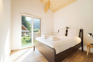 A bedroom with a bed, bedside tables, and a view of a garden through a sliding door. - Cimes - Modern, Sleeps 8 | New | Family-Friendly | Quiet Location (Chamonix)