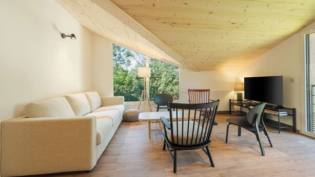 Un salon moderne avec un canapé, des fauteuils, un téléviseur et une lampe.