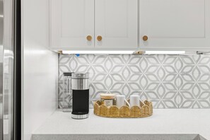 A kitchen with white cabinets, a stainless steel coffee maker, a basket with jars, and a patterned backsplash. - Stylish 3-bedroom house in Houston Great Location - Near Med Center, Energy (Houston)
