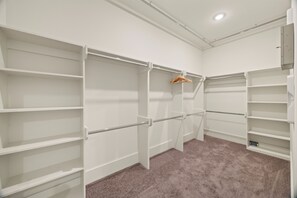 Un dressing accessible sans porte, doté d’étagères ouvertes, d’une tringle et d’un sol recouvert de moquette.