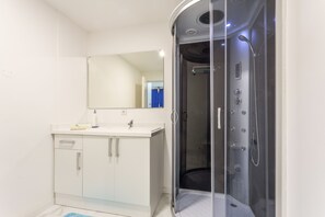A modern bathroom with a white vanity, a mirror, and a glass-enclosed shower stall. - Open-space Hostel for Groups – Near Ericeira and Mafra (Mafra)