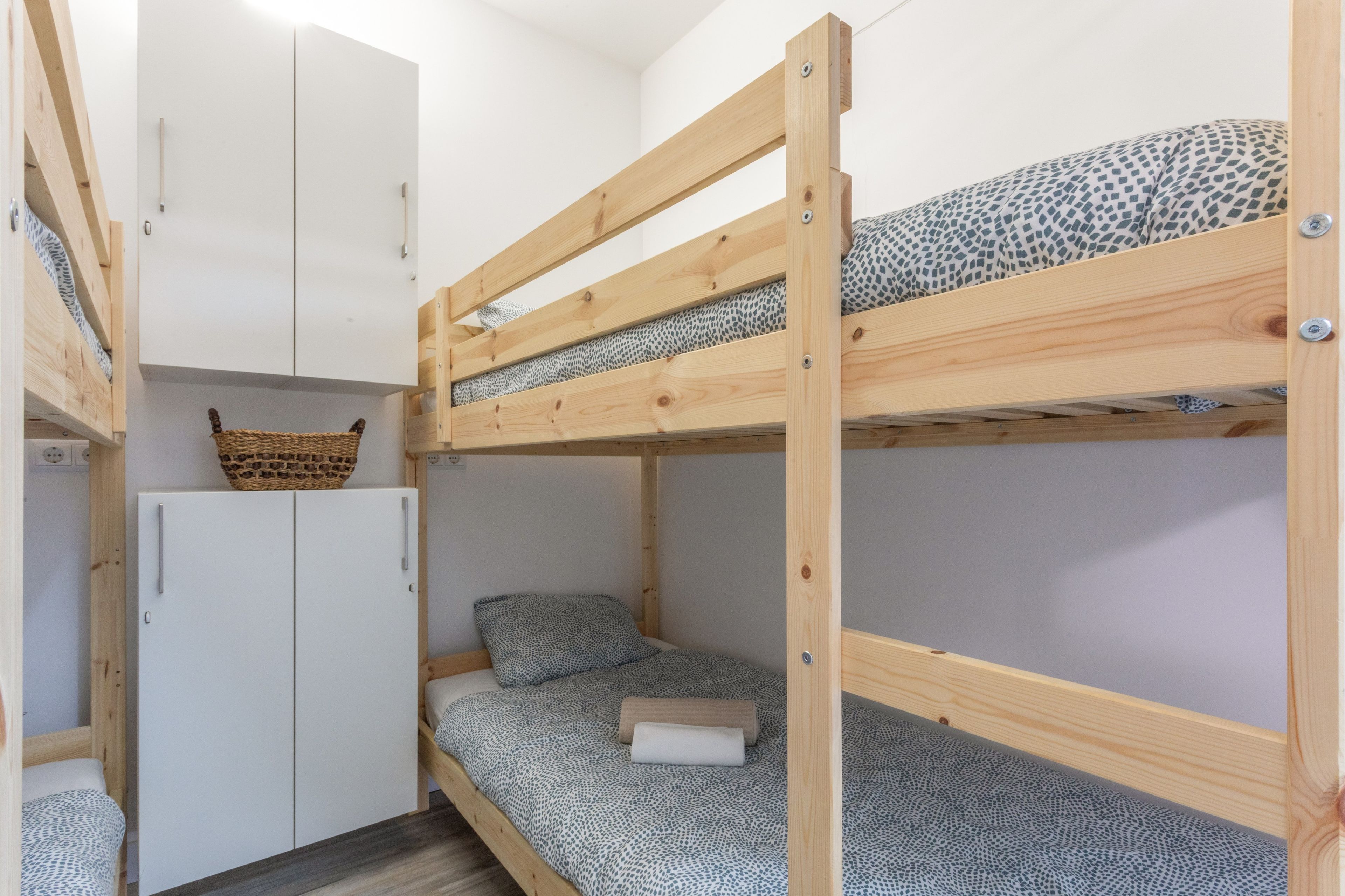 Una cama individual con estructura de madera, un armario blanco y una cesta tejida encima.
