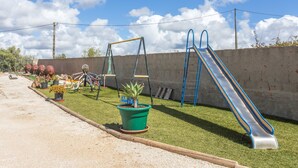 Un terrain de jeux avec des balançoires, un toboggan et une petite plante verte.