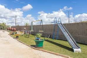 Ein Spielplatz mit Schaukeln, einer Rutsche und einer kleinen grünen Pflanze.