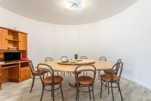 Ein Essbereich mit einem runden Holztisch, sechs Stühlen, einem Fernseher auf einer Holzkommode und einer weißen Wand.