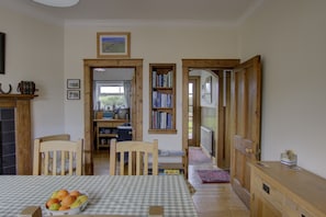 A dining area with a checkered tablecloth, wooden chairs, a fruit bowl, and a bookshelf with books. - Benarty, a cosy one-bedroom property in Brora. (Brora)