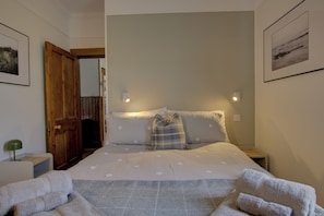 Ein Schlafzimmer mit einem Bett, zwei Nachttischen, einer Kommode, einer Holztür und einem gerahmten Bild an der Wand.