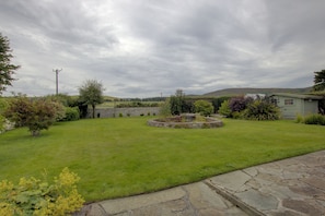 A well-maintained lawn with a stone circular feature, possibly a fountain, surrounded by a variety of shrubs and trees. - Benarty, a cosy one-bedroom property in Brora. (Brora)