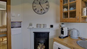 Una cucina con una sveglia a parete, una macchina da caffè e un pensile con vetri.