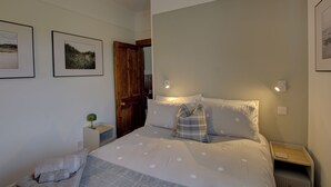 Una camera da letto con un letto, un comodino, una lampada, una porta e due quadri appesi al muro.