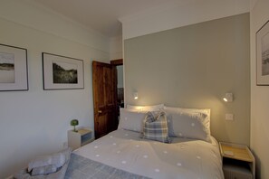 A bedroom with a bed, a nightstand, a lamp, a door, and two framed pictures on the wall. - Benarty is a charming one‑bedroom cottage set on the edge of the peaceful village of Brora (Brora)