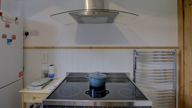 Una cucina con un fornello, una pentola sul fuoco, un forno a incasso e una porta in legno.