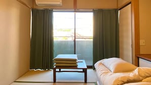 Una habitación con cama, una mesita con un cojín y una puerta corredera que da a un espacio exterior.