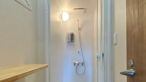 Un pasillo estrecho que conduce a un área de ducha con una puerta a la derecha, una lámpara sobre la ducha y un perchero a la izquierda.