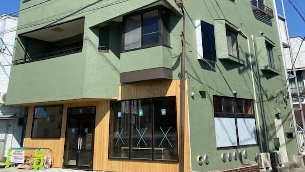 Un edificio de varios pisos con tejado plano, ventanas amplias y fachada verde.
