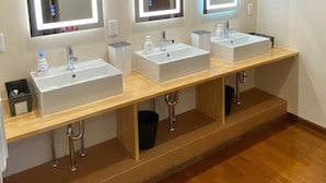 Un baño moderno con tres lavamanos, cada uno con espejo e iluminación bajo el mueble.