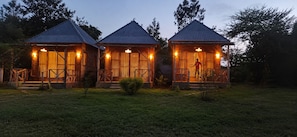 Three wooden cabins with metal roofs, each with a porch and a staircase leading to the entrance. - Oloresho Safari Lodge (Arusha)