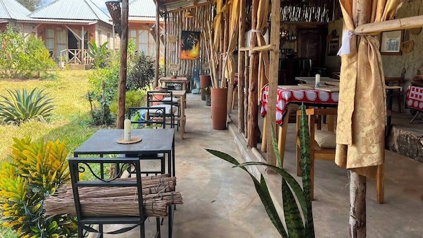 Área externa com mesas e cadeiras, cercada por plantas e vista para uma casa.