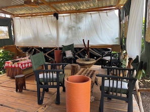 An outdoor seating area with wooden furniture, a large terracotta pot, and a covered space with a white canopy. - Oloresho Safari Lodge (Arusha)