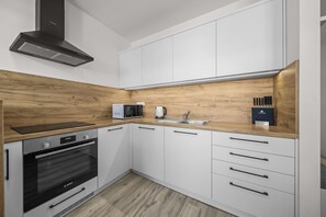 Moderni keittiö, jossa on valkoiset kaapit, Bosch-uuni, mikroaaltouuni ja pesuallas.