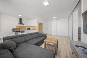 Ein modernes Wohnzimmer mit einem grauen Ecksofa, einem Couchtisch aus Holz und einer TV-Konsole mit Fernbedienung.
